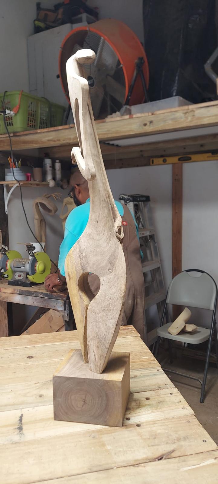 Escultura de madera sobre el banco del taller con herramientas y esmeriladora al fondo